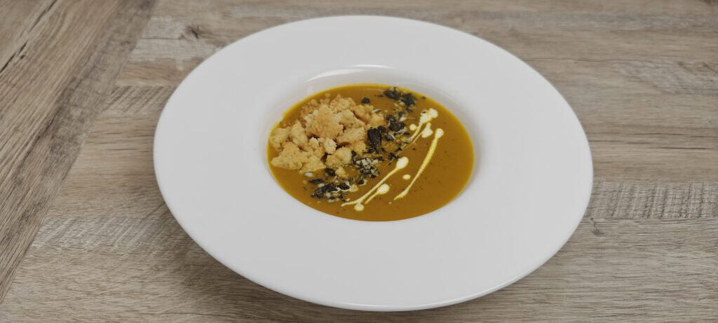 Creamy pumpkin soup in a white bowl with Parmesan crumble, pumpkin seeds and a swirl of cream.
