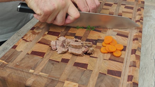 Cooked beef and carrots being sliced with fresh parsley for beef soup