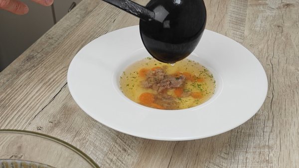 Hot homemade beef soup being ladled over beef, carrots and dumplings