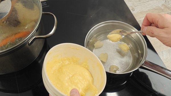Soft dumpling dough being shaped with a teaspoon over simmering water