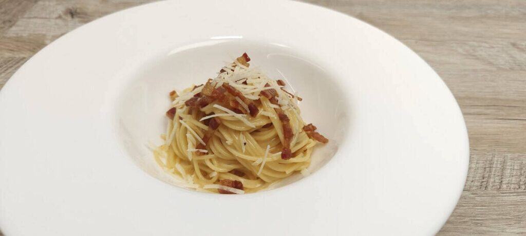 Creamy spaghetti carbonara topped with crisp pancetta, Parmesan and black pepper on a white plate