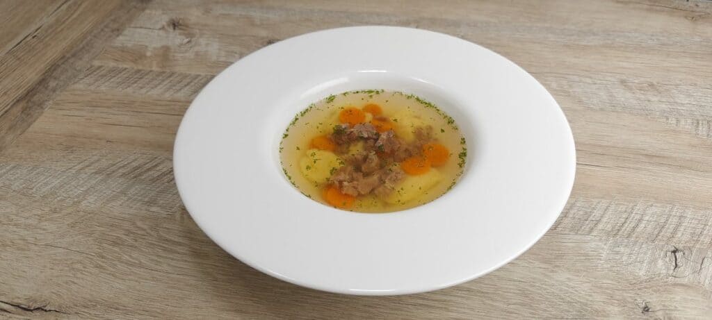 Homemade beef soup with beef, carrots and soft dumplings in a white bowl